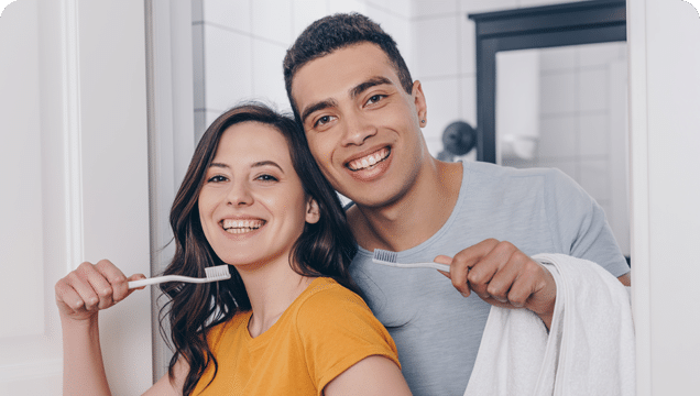 A smiling couple holds toothbrushes, showcasing their joyful routine of brushing teeth together