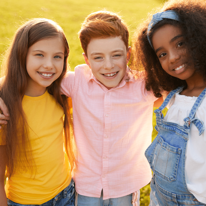 Three young friends standing together in a field, enjoying a sunny day and sharing smiles